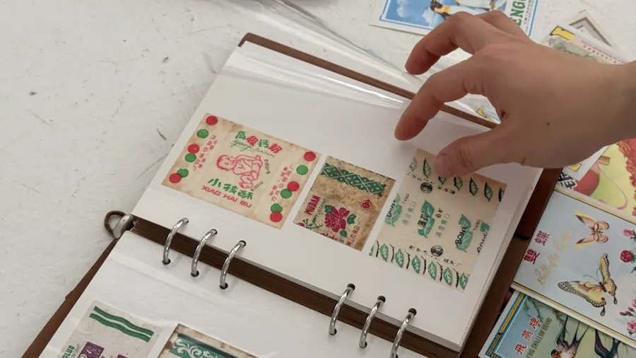 A hand turning through an archive binder of collected paper objects.